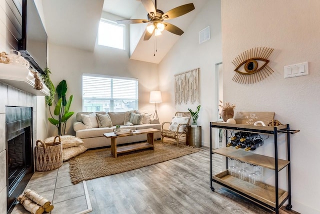 living room with a wealth of natural light, visible vents, a tiled fireplace, and wood finished floors