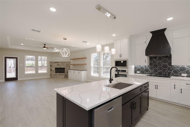 kitchen featuring sink, custom exhaust hood, a stone fireplace, stainless steel appliances, and a kitchen island with sink