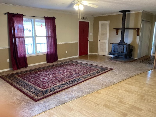 unfurnished living room with a wood stove, wood-type flooring, ornamental molding, and ceiling fan