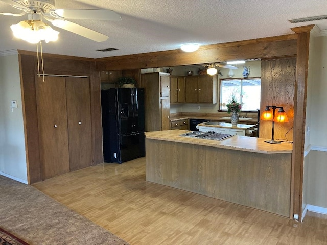 kitchen with a textured ceiling, black refrigerator with ice dispenser, kitchen peninsula, and light hardwood / wood-style flooring