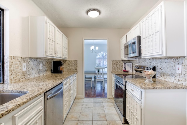 kitchen featuring appliances with stainless steel finishes, white cabinetry, light stone counters, and an inviting chandelier