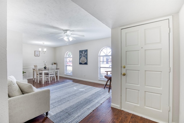 foyer entrance featuring dark wood-style flooring, a textured ceiling, baseboards, and ceiling fan with notable chandelier