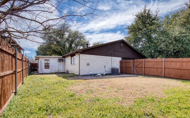 rear view of house featuring brick siding, a lawn, board and batten siding, cooling unit, and a fenced backyard