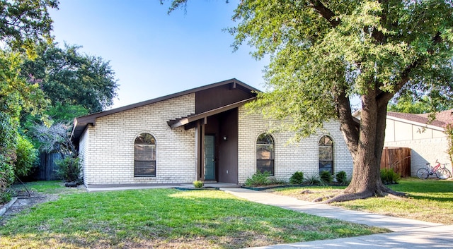 mid-century inspired home featuring brick siding, a front yard, and fence