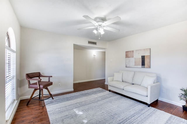 living area featuring dark wood-type flooring, visible vents, baseboards, and a ceiling fan