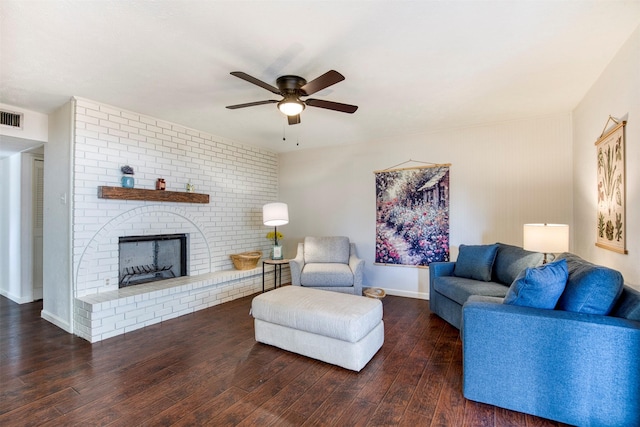 living area featuring dark wood finished floors, visible vents, a ceiling fan, a brick fireplace, and baseboards