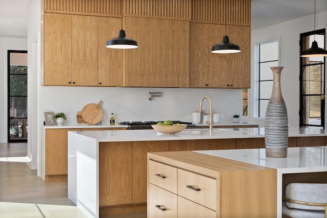 kitchen with light wood-type flooring, decorative backsplash, a kitchen island with sink, and decorative light fixtures