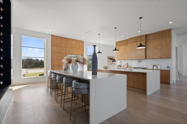 kitchen with sink, a large island, hanging light fixtures, and light hardwood / wood-style flooring