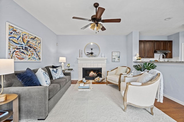 living area with light wood-type flooring, a fireplace, a ceiling fan, and baseboards