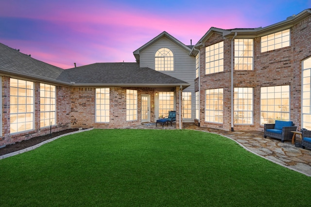 rear view of property with a yard, a shingled roof, and brick siding