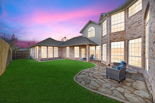 rear view of property featuring brick siding, a patio, a fenced backyard, and a lawn