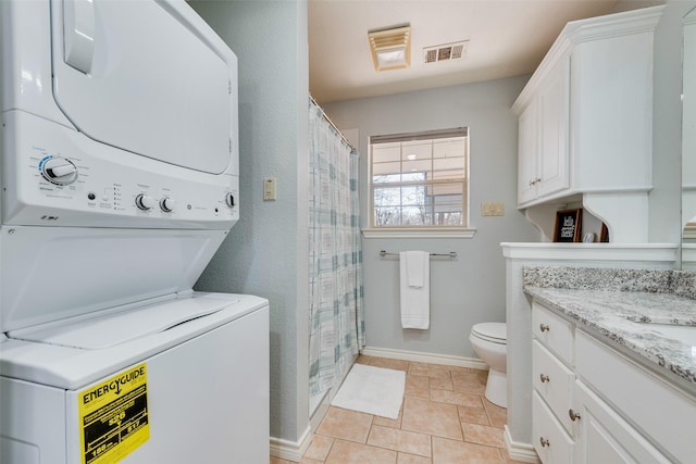 laundry area with stacked washer and dryer and light tile patterned floors