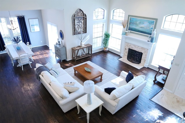 living room featuring an inviting chandelier, dark wood-type flooring, a high ceiling, and a fireplace