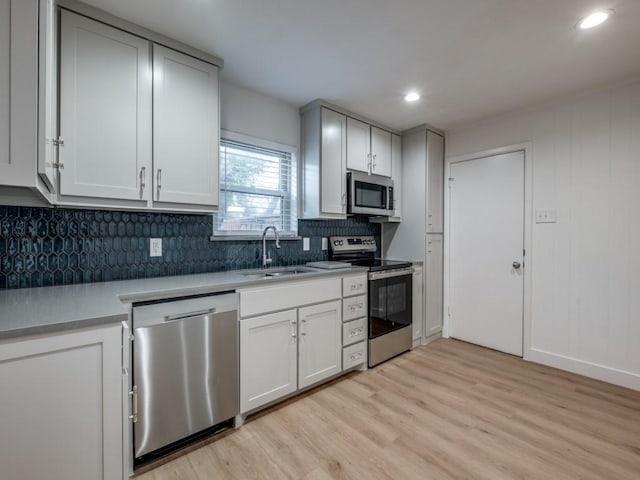 kitchen featuring appliances with stainless steel finishes, light hardwood / wood-style flooring, white cabinets, decorative backsplash, and sink