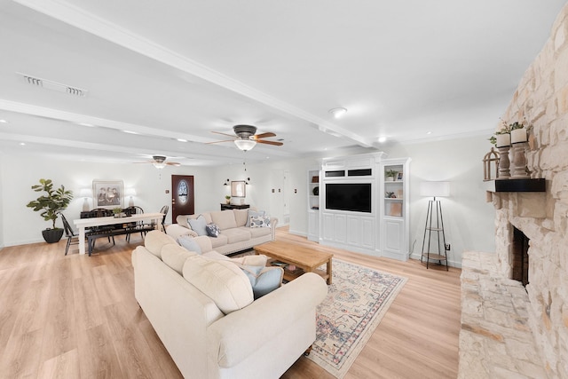 living room featuring beam ceiling, ceiling fan, light hardwood / wood-style floors, and a stone fireplace