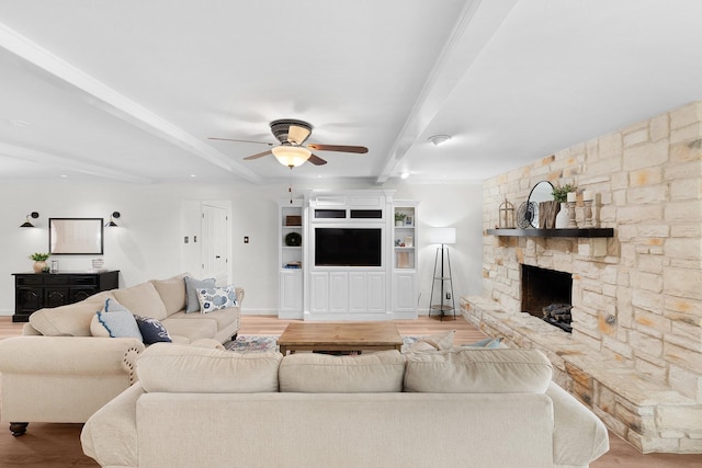 living room featuring ceiling fan, beamed ceiling, a stone fireplace, and light hardwood / wood-style flooring