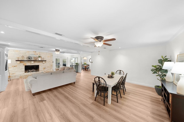 dining area with ceiling fan, a stone fireplace, and light hardwood / wood-style flooring