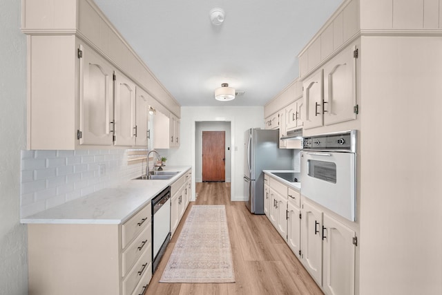 kitchen featuring light hardwood / wood-style flooring, dishwashing machine, decorative backsplash, sink, and white oven