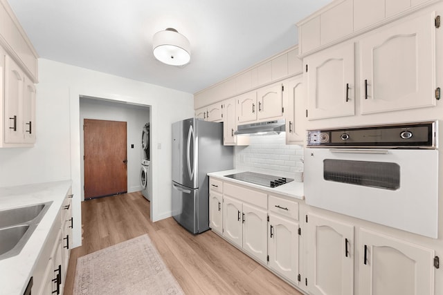 kitchen featuring light wood-type flooring, black appliances, stacked washer / dryer, tasteful backsplash, and white cabinets