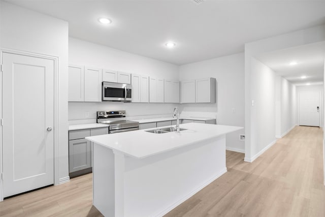 kitchen featuring appliances with stainless steel finishes, a kitchen island with sink, light countertops, light wood-type flooring, and a sink