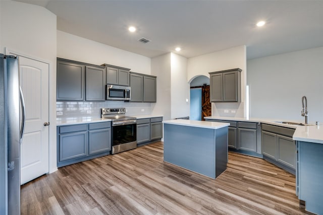 kitchen featuring arched walkways, wood finished floors, a sink, light countertops, and appliances with stainless steel finishes