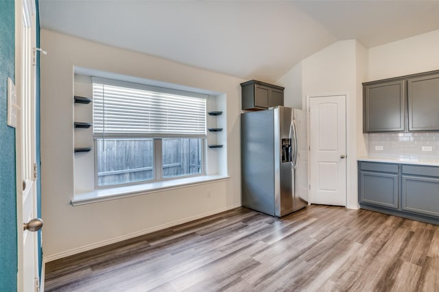 kitchen featuring gray cabinets, light countertops, backsplash, vaulted ceiling, and stainless steel fridge with ice dispenser