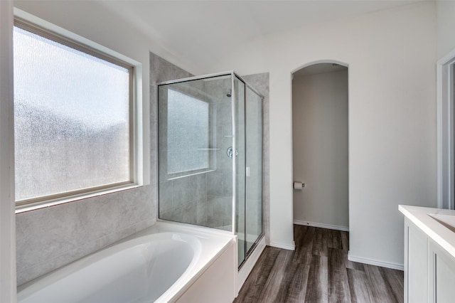 bathroom with a garden tub, wood finished floors, vanity, baseboards, and a stall shower