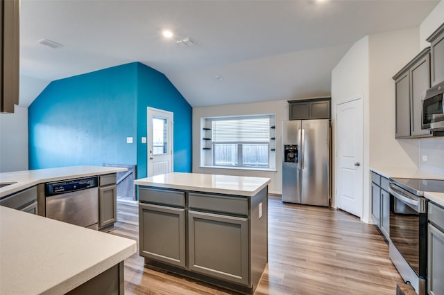 kitchen with lofted ceiling, gray cabinetry, light countertops, appliances with stainless steel finishes, and a center island