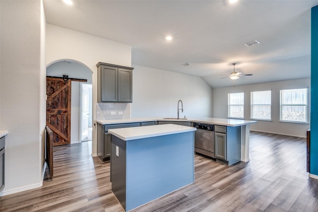 kitchen with a barn door, a peninsula, light countertops, a center island, and dishwasher