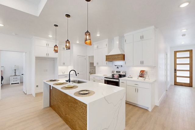 kitchen with a center island with sink, electric stove, sink, custom exhaust hood, and white cabinetry