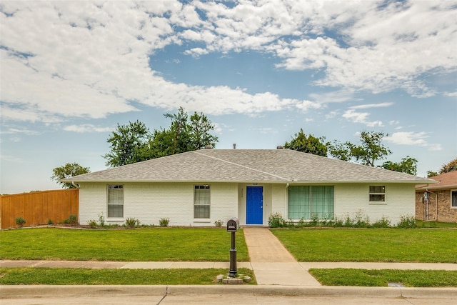 ranch-style home featuring a shingled roof, fence, a front lawn, and brick siding