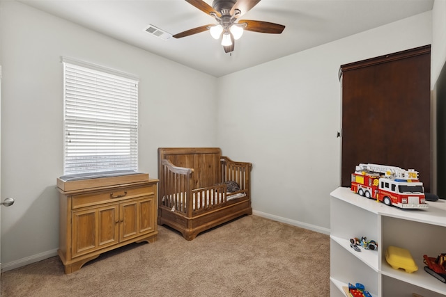 carpeted bedroom featuring ceiling fan and a crib