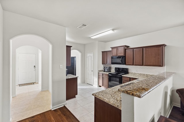 kitchen featuring kitchen peninsula, dark brown cabinetry, black appliances, light stone counters, and light tile patterned flooring