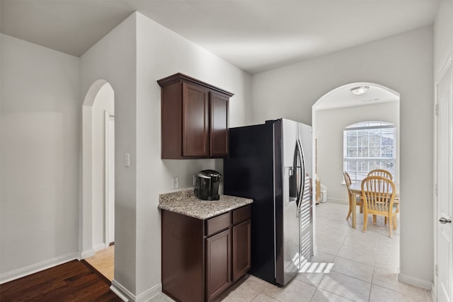kitchen with dark brown cabinetry, light stone countertops, and stainless steel refrigerator with ice dispenser