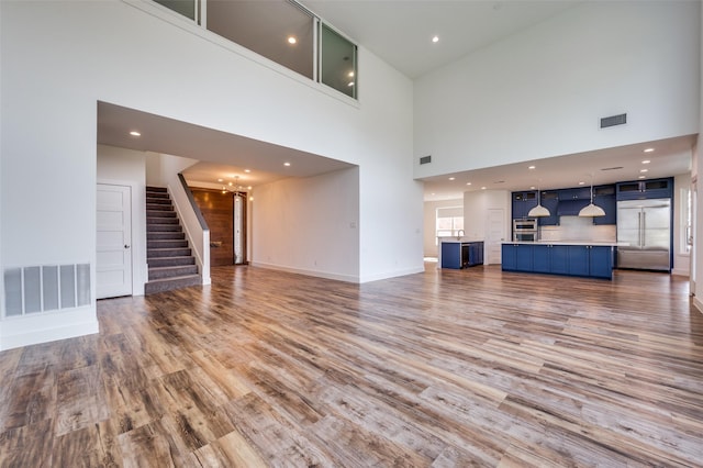 unfurnished living room featuring stairs, light wood finished floors, visible vents, and baseboards