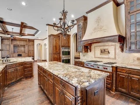 kitchen featuring arched walkways, custom range hood, a kitchen island, glass insert cabinets, and a sink