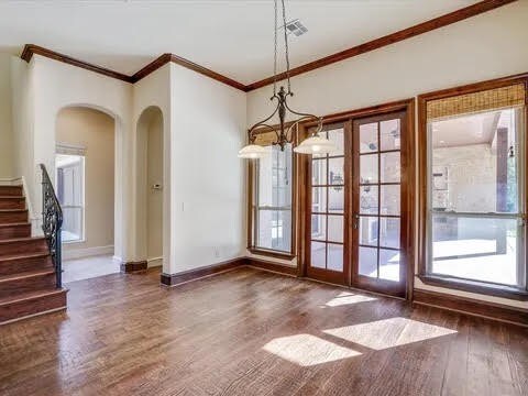 unfurnished dining area featuring baseboards, dark wood finished floors, arched walkways, ornamental molding, and stairs