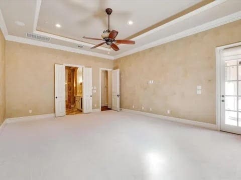 unfurnished bedroom with baseboards, visible vents, a tray ceiling, and crown molding