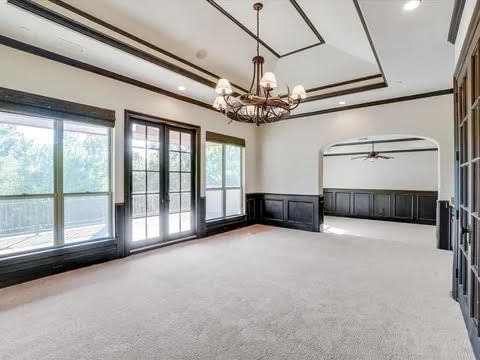 empty room with ornamental molding, light colored carpet, wainscoting, and a tray ceiling