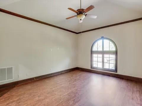 empty room with crown molding, visible vents, ceiling fan, wood finished floors, and baseboards