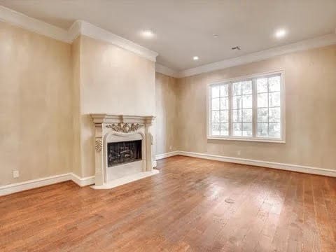 unfurnished living room with crown molding, a fireplace, baseboards, and wood finished floors