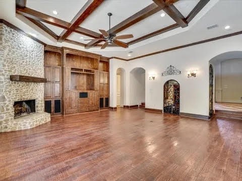 unfurnished living room featuring a ceiling fan, arched walkways, beam ceiling, and coffered ceiling