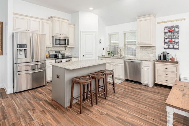 kitchen featuring stainless steel appliances, light stone countertops, a center island, and lofted ceiling