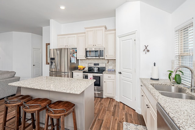 kitchen with stainless steel appliances, a breakfast bar area, light stone countertops, sink, and dark hardwood / wood-style floors