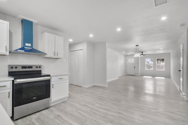 kitchen with wall chimney range hood, stainless steel range with electric cooktop, white cabinetry, and light hardwood / wood-style floors