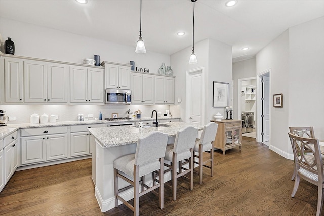 kitchen with stainless steel appliances, a kitchen island with sink, pendant lighting, and light stone counters