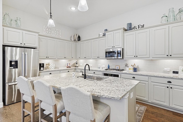 kitchen with a center island with sink, sink, pendant lighting, stainless steel appliances, and white cabinets