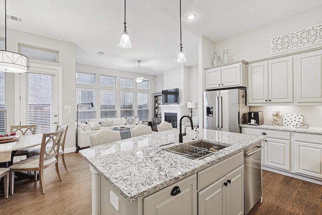 kitchen with appliances with stainless steel finishes, an island with sink, decorative light fixtures, dark hardwood / wood-style flooring, and sink