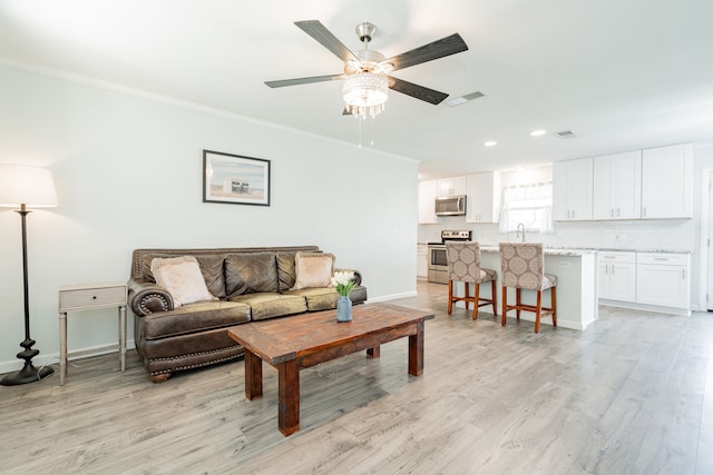 living room with crown molding, light wood-style flooring, baseboards, visible vents, and ceiling fan