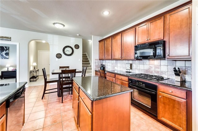 kitchen featuring dark stone counters, black appliances, a center island, backsplash, and light tile patterned floors